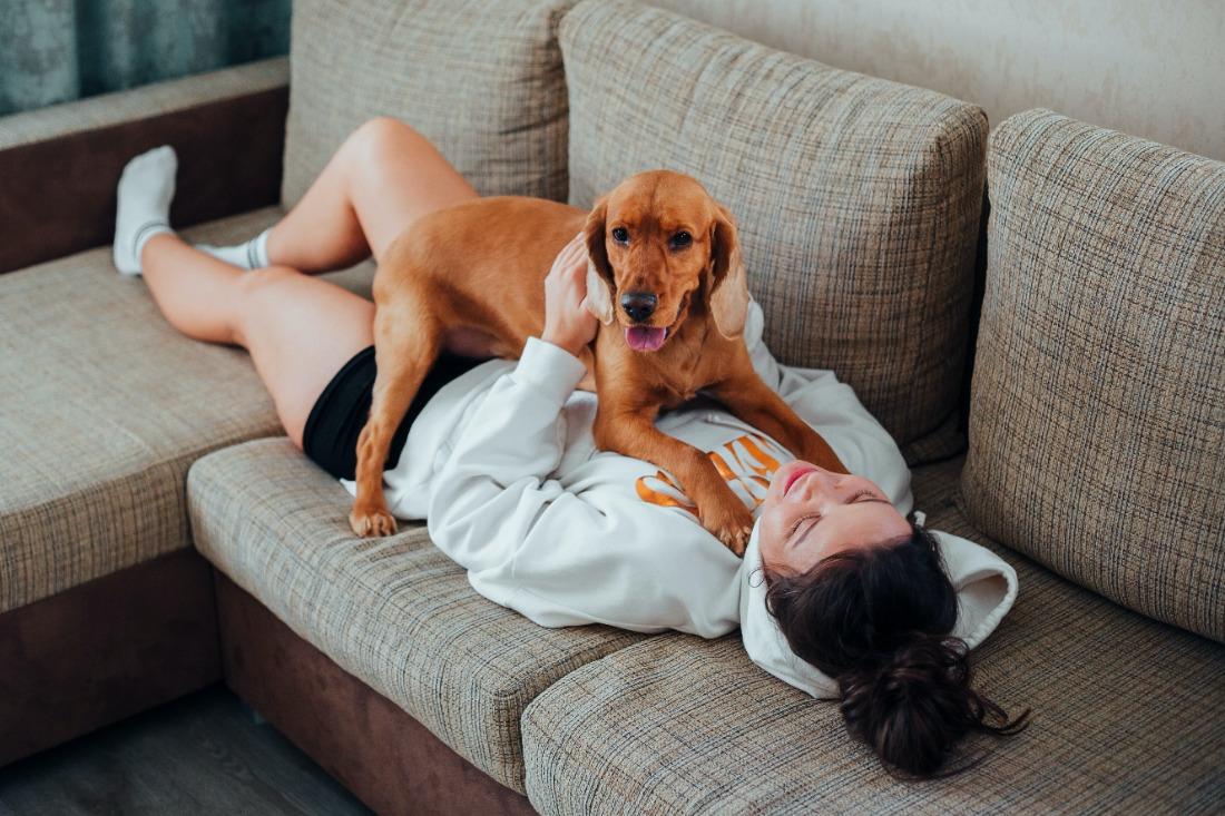 une fille allongé sur un canapé s'amuse avec son chien